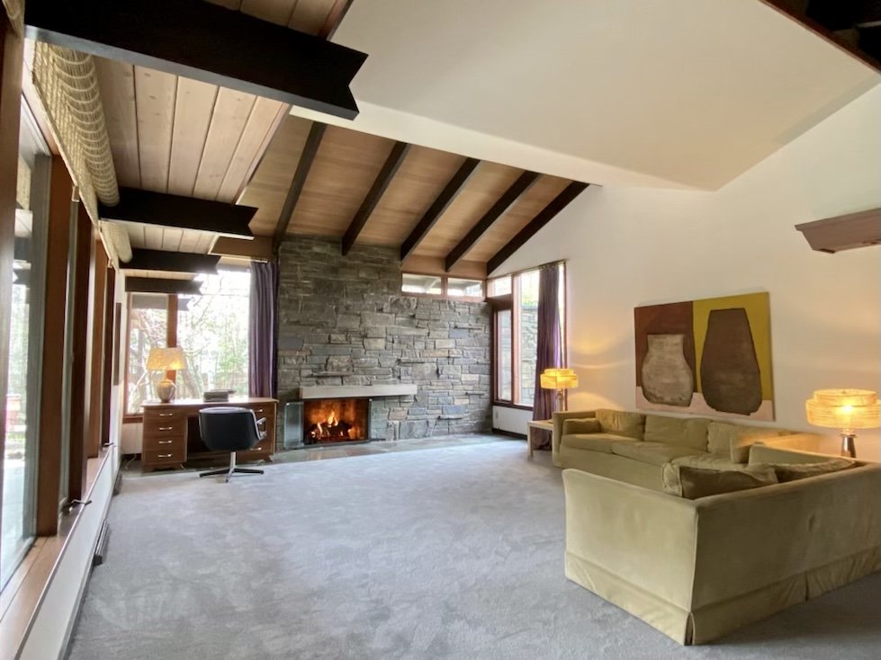 Cozy living room with plush carpet, stone fireplace, and large windows